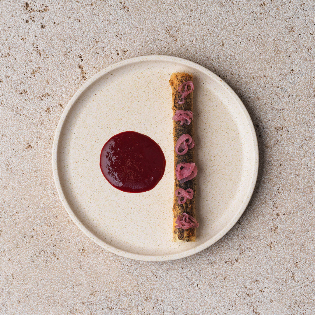 Elegant plate presentation of a modern dish, with a crimson sauce and thinly sliced garnish, showcased on a minimalist plate.