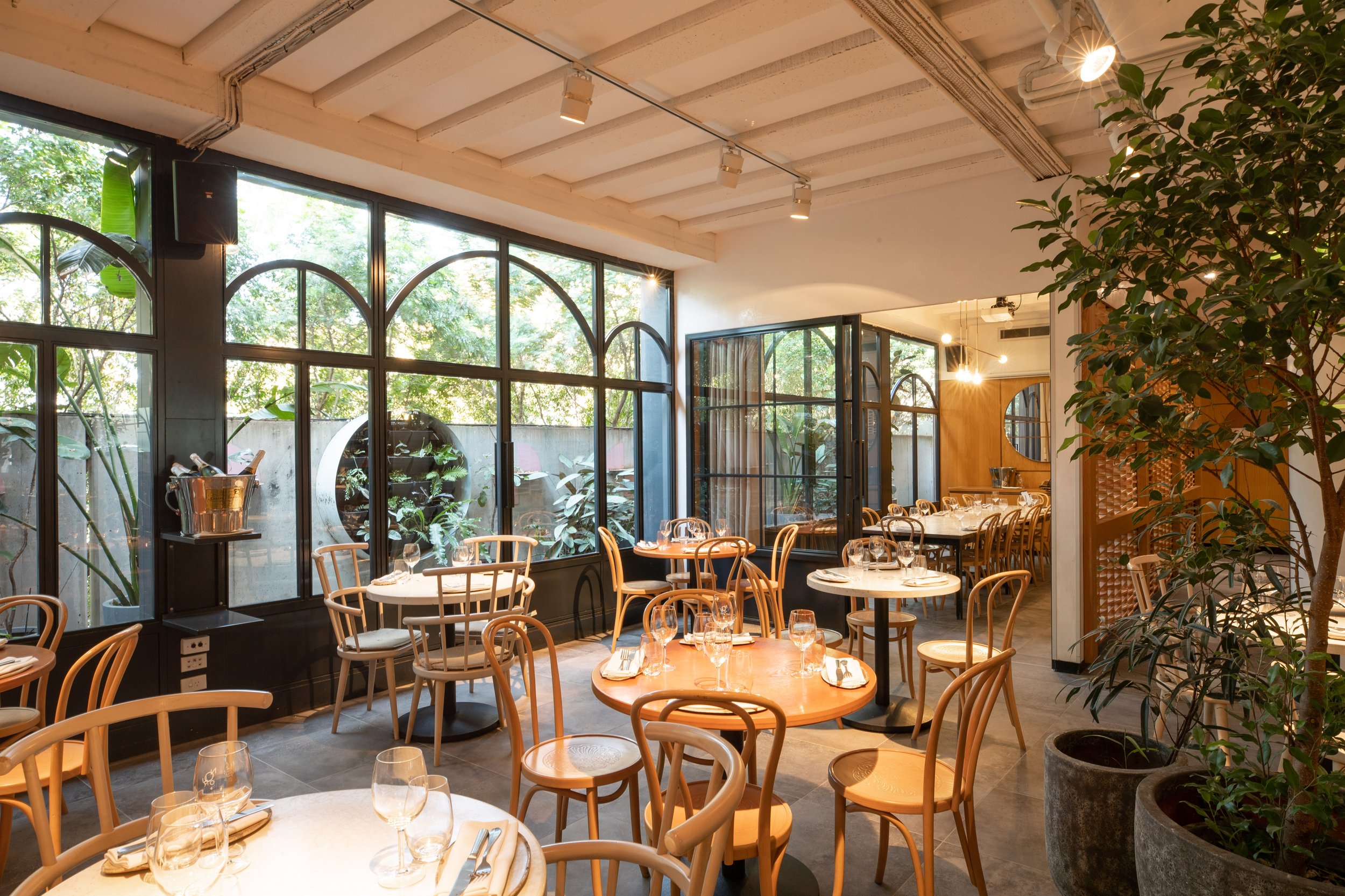 Bright, airy dining space at Nour restaurant with modern decor, wood accents, and large arched windows overlooking greenery.