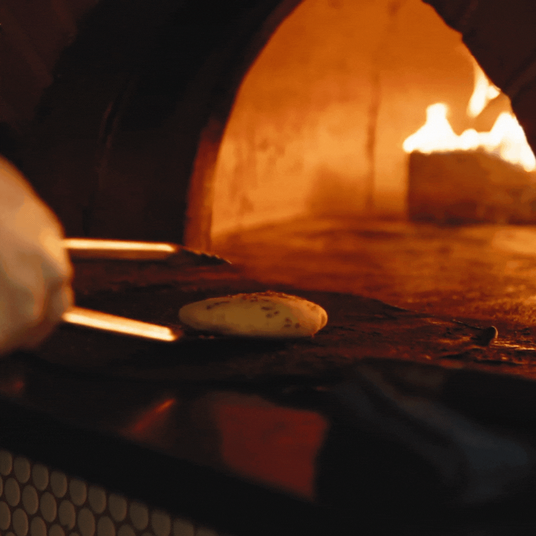 promotional material for NOUR Restaurant Sydney's one-off dinner with Four Pillars, bread being taken out of a fire-lit brick oven