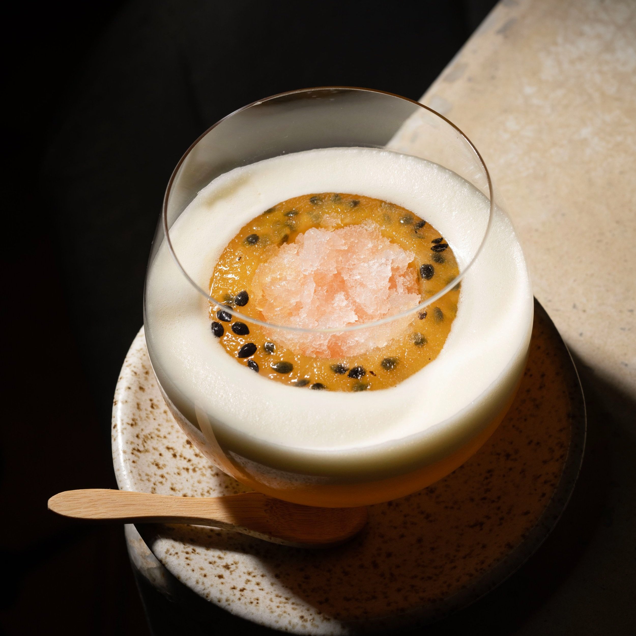 An elegant dessert in a glass featuring a scoop of pink sorbet topped with passionfruit seeds