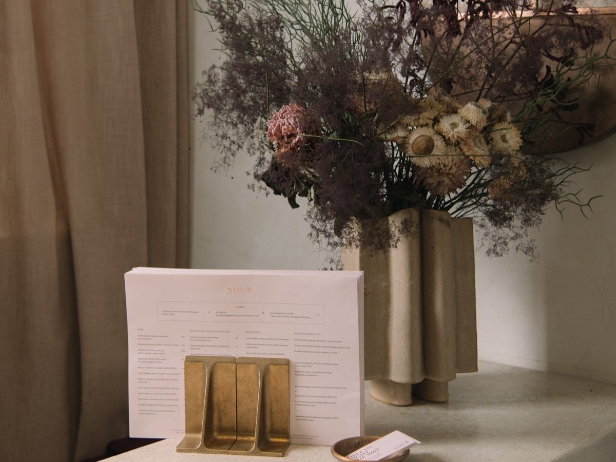 A carner at NOUR Restaurant Sydney, featuring an elegant menu on a marble table, complemented by a unique floral arrangement in a modern sculptural vase