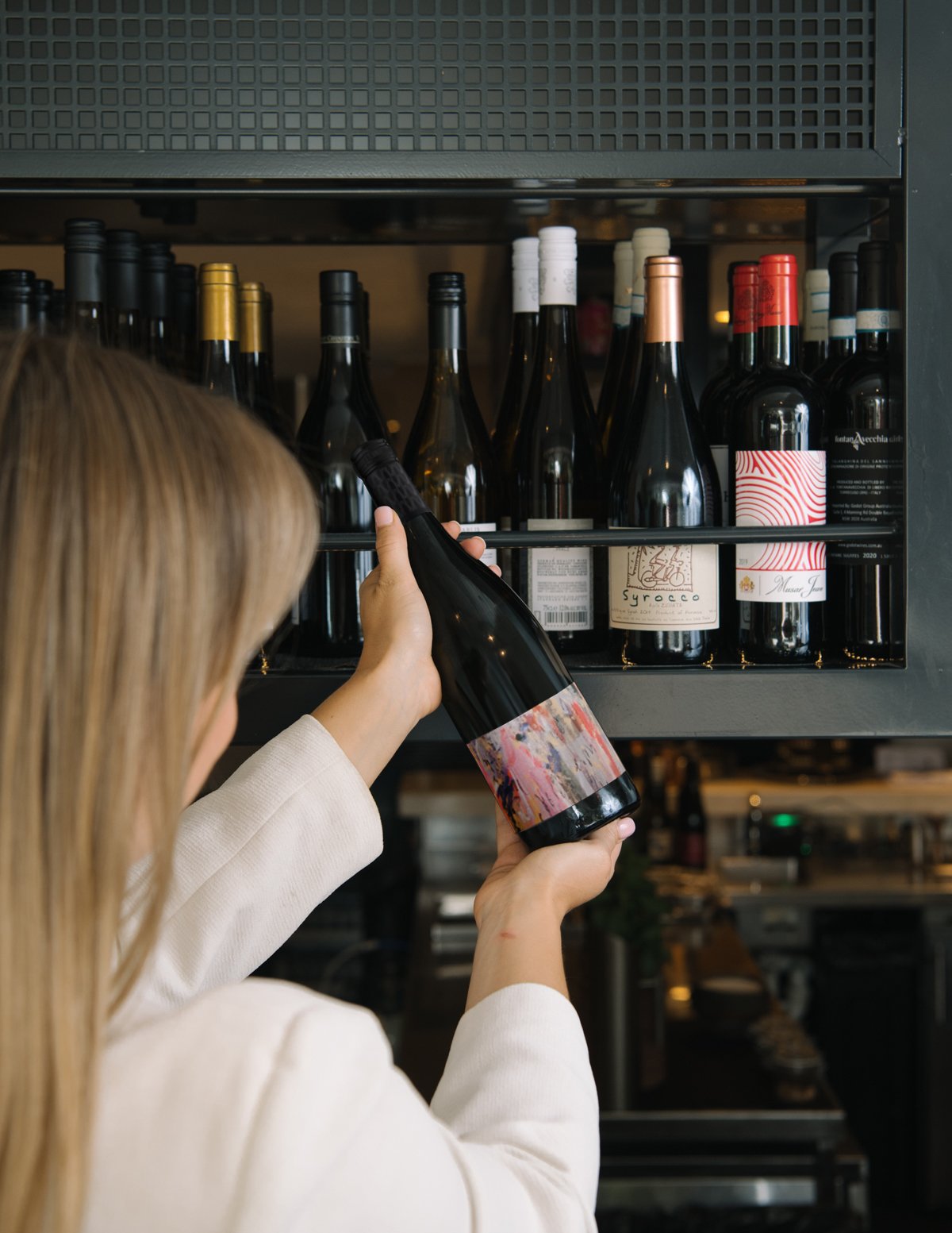 NOUR Restaurant Sydney promotional material introducing the 2022 Single Vineyard release from Mulline. image depicts woman in white blouse with back against the camera, holding a bottle of wine