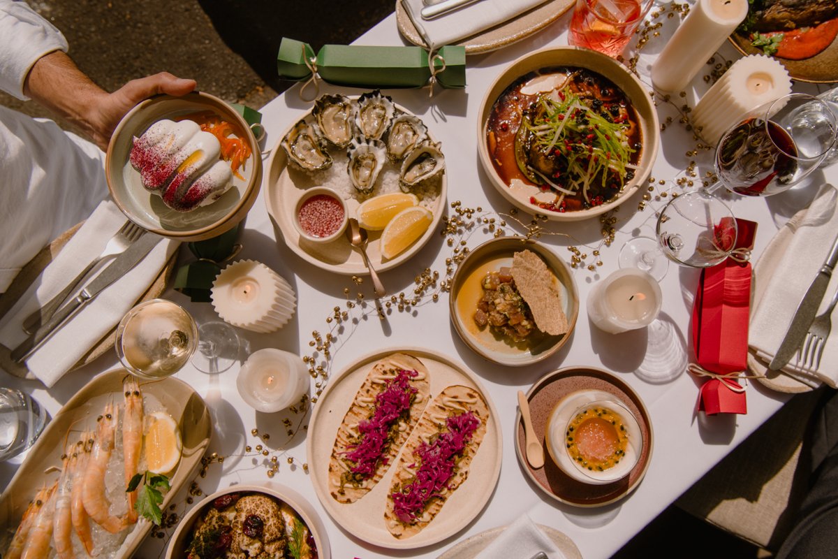 A festive table spread featuring a variety of dishes such as prawns, oysters, and a bowl of caviar, desserts, and various dishes